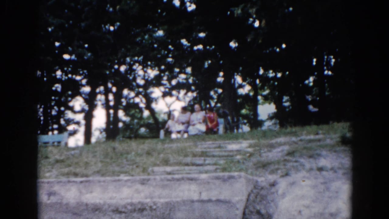 Two figures in summer clothing resting on stone park terracing in Illinois, circa 1962, captured on 8mm home movie film.