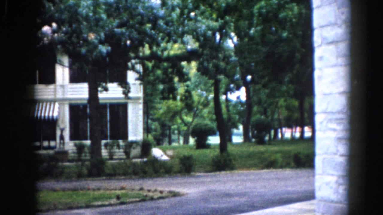 Camera panned right to show white clapboard house with striped awning and a stone architectural element at the right frame edge.