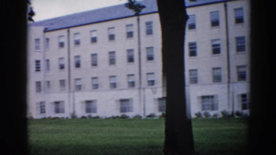 Four-story institutional building extends across frame on Illinois campus, circa 1962; repeating window bays and flat roof with blue-gray trim visible in mid-pan.