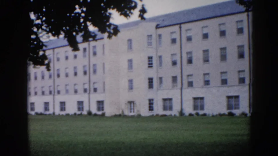 End of slow pan across four-story institutional building on Illinois campus, circa 1962; leafy tree now visible at upper right alongside the repeating window grid.