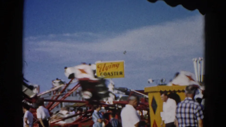 'Flying Coaster' ride with gondola cars and red metal structure at an outdoor fairground, consistent with Illinois circa 1962; yellow brand sign prominent under blue sky