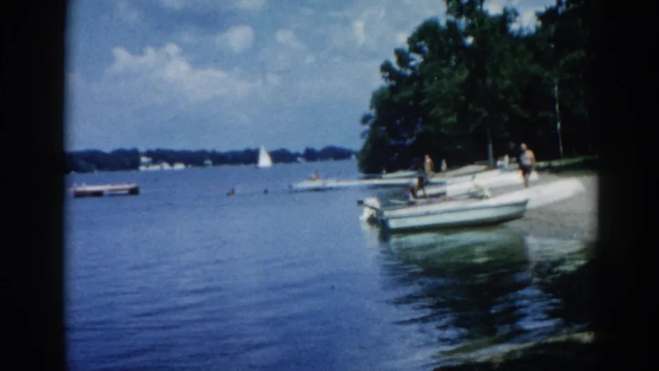 Two or three adults preparing to board a motorboat on an Illinois lake, circa 1962, with sailboats visible in the distance.
