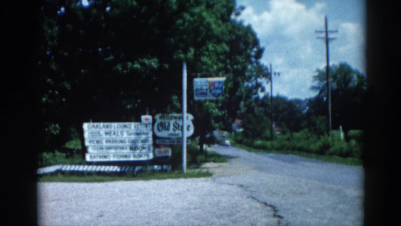 Roadside sign cluster for Oakland Lounge Resort and Old Style beer brand beside a gravel road lined with trees.