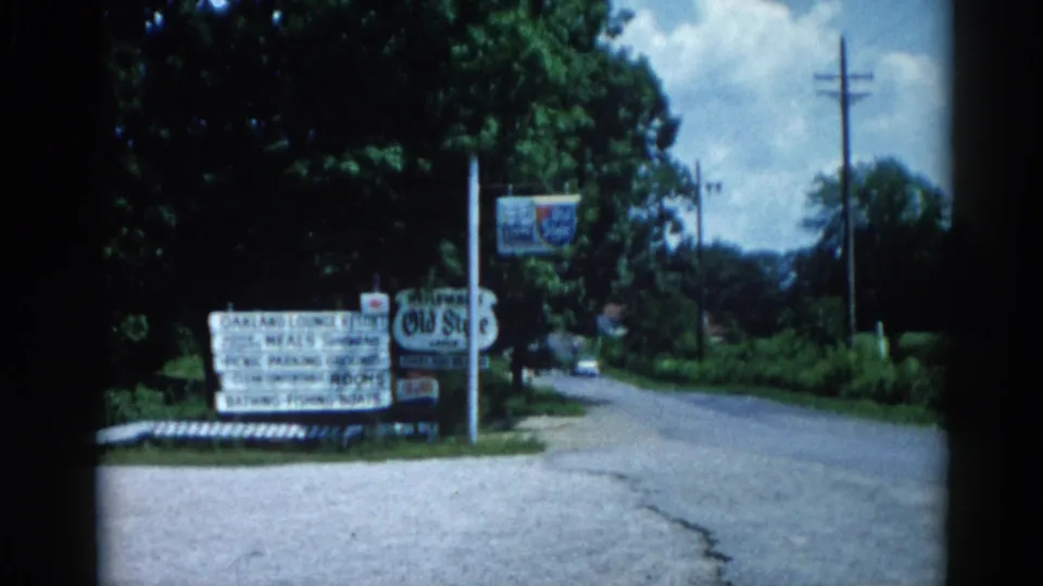 Illinois roadside circa 1962: resort signs listing meals, rooms, boats, and bathing, with apparent Old Style beer branding visible, blue sky, and summer foliage.