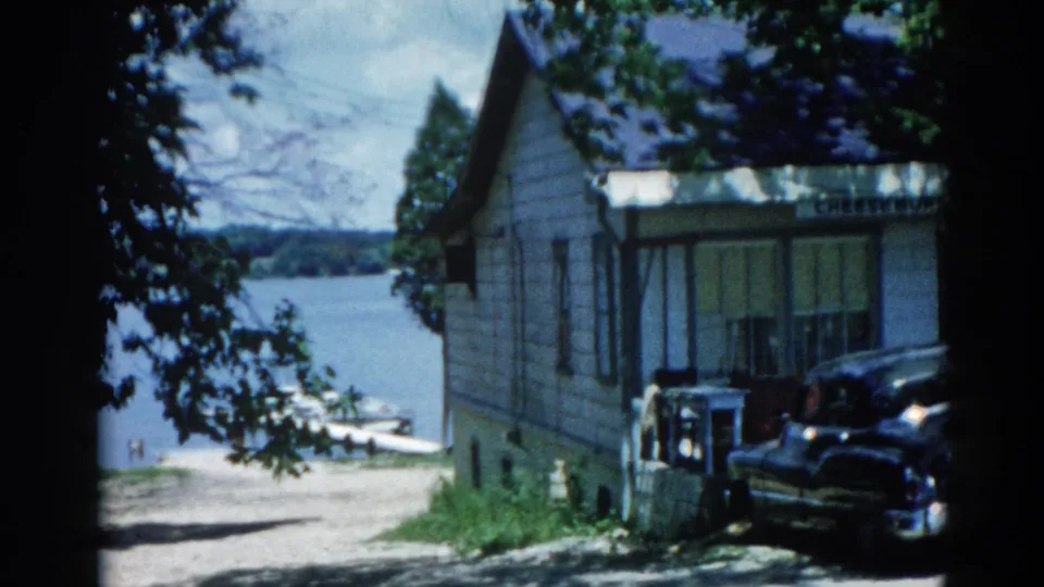 Second 8mm frame from 1962 Illinois showing the same lakeside house and grounds with a dark period automobile parked alongside.