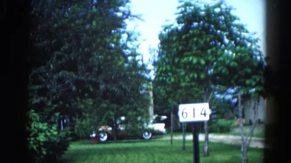 Suburban front yard in Illinois, circa 1962 — address sign '614' on a post, early-1960s American car with whitewall tires, framed by mature deciduous trees.