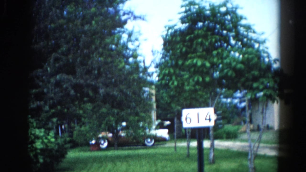 Continuation of the Illinois suburban establishing shot, circa 1962, with address marker '614' and classic car visible under full tree canopy.