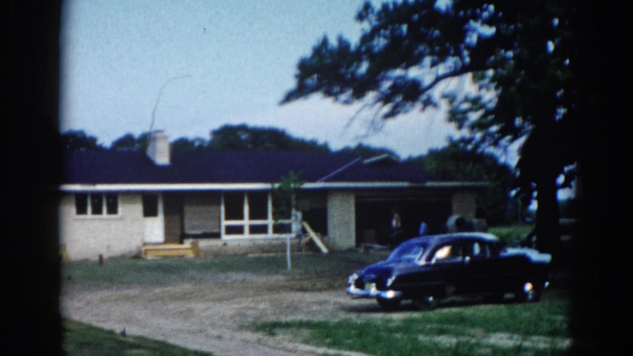 Nearly identical static view of ranch home and dark sedan; composition matches preceding frame with minimal camera movement.