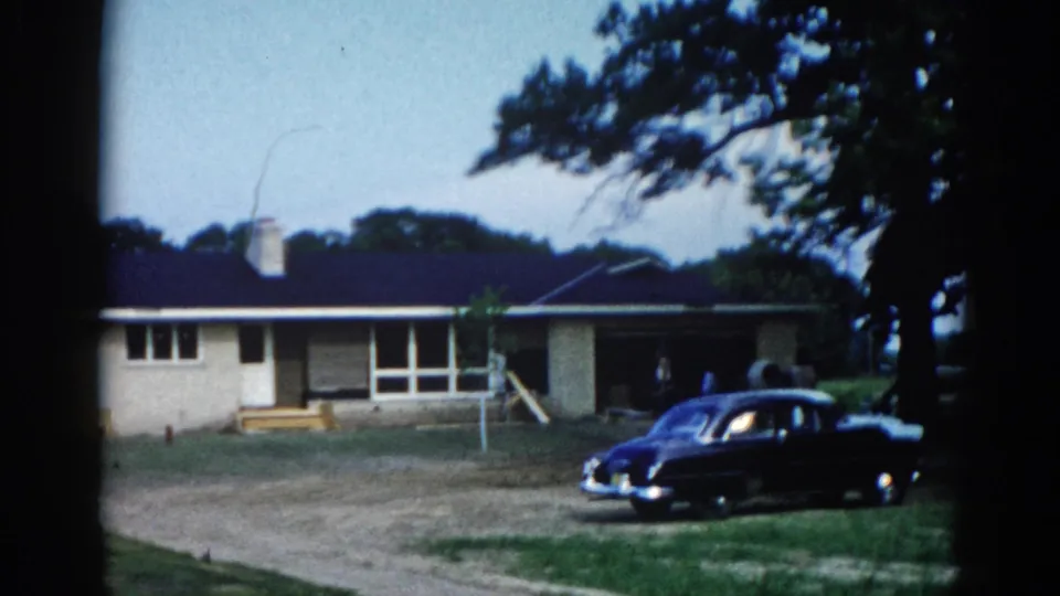 Static 8mm shot of a ranch-style home and dark classic American sedan, Illinois circa 1962; scene virtually unchanged from first frame, confirming a held static shot.