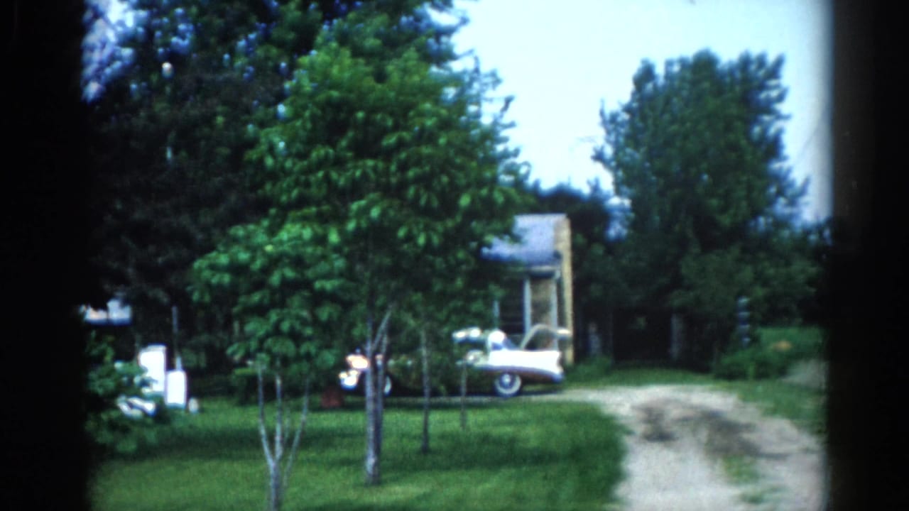 Suburban yard with a white classic car on a gravel driveway, a modest house with covered porch, and large deciduous trees.