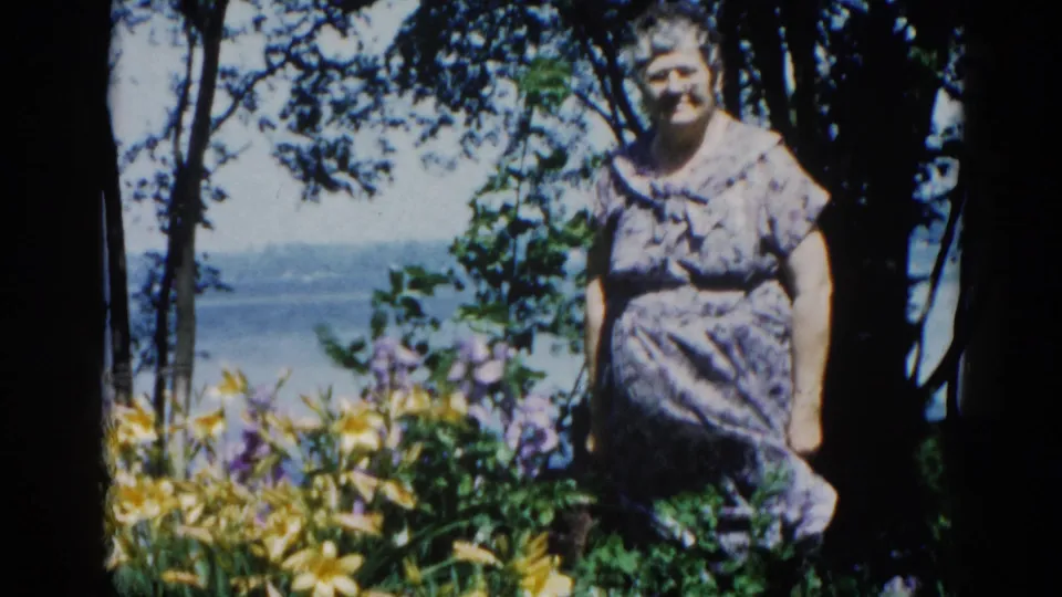 Final frame of elderly woman in lakeside garden, 8mm color footage with visible grain, natural light, Illinois circa 1962.