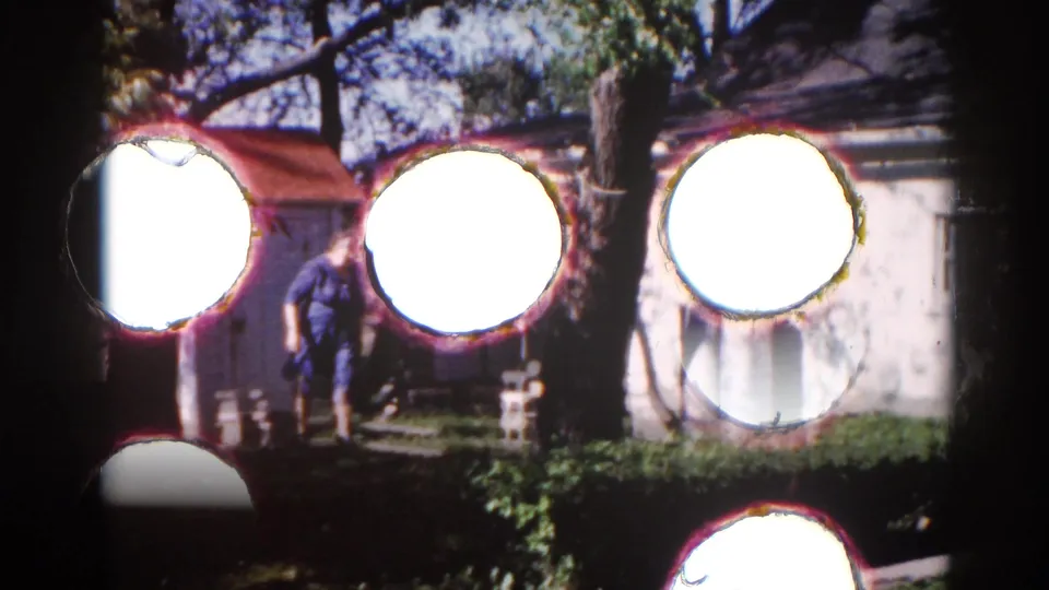 Severe lens flares from direct sunlight nearly obscure the scene; a figure near a white outbuilding is partially visible, Illinois circa 1962.