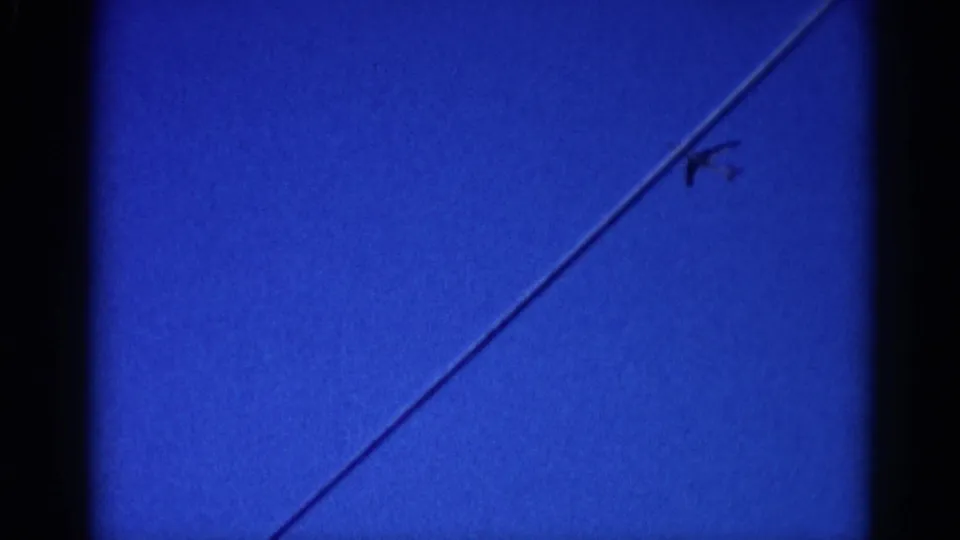8mm home movie frame, circa 1962, Illinois — clear blue sky with a single diagonal jet contrail stretching across the frame.