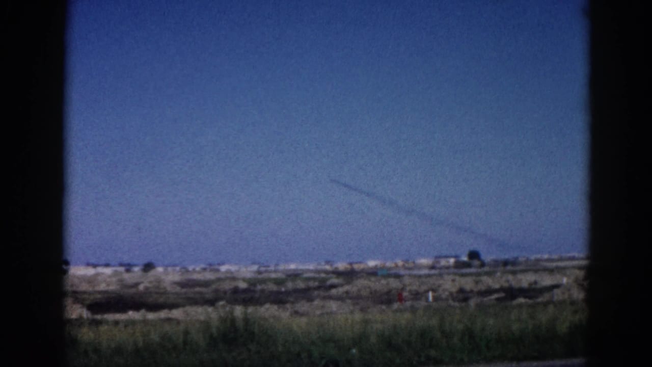View through a car window of flat rural landscape under a wide blue sky with a thin contrail visible