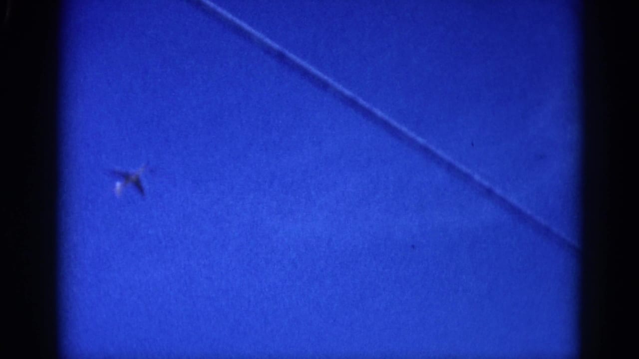 Small aircraft and a diagonal overhead wire crossing an 8mm-filmed blue sky, circa 1962 Illinois.
