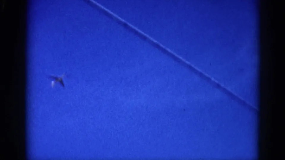 Small aircraft and a diagonal overhead wire crossing an 8mm-filmed blue sky, circa 1962 Illinois.