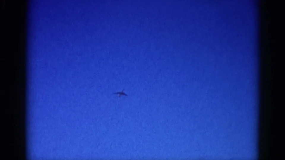 Jet aircraft silhouette in lower frame area, crossing a clear blue sky on 8mm film, Illinois circa 1962.