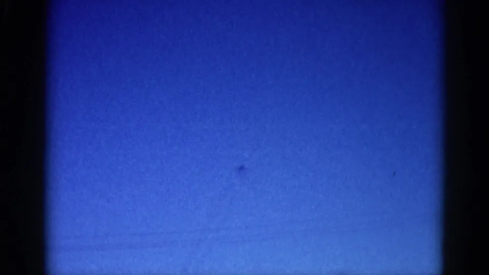 8mm home movie frame, circa 1962 Illinois: more saturated blue sky with a barely-visible aircraft speck and subtle horizontal film marks.