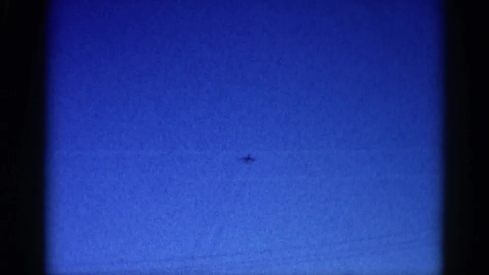 8mm home movie final frame, circa 1962 Illinois: vivid deep blue sky, barely-visible distant aircraft, and film-surface marks consistent with aged stock.