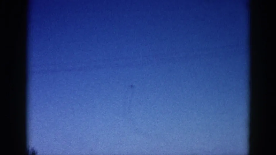8mm home-movie frame circa 1962, Illinois: deep blue dusk sky with a small aircraft silhouette, visible film grain, and dark vignette framing.