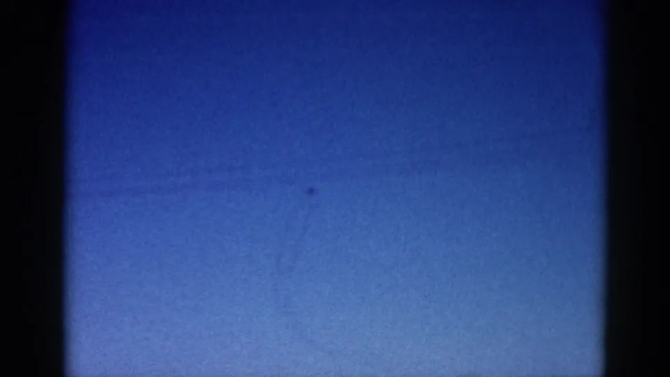 8mm archival frame circa 1962 showing deep blue twilight sky with a distant aircraft and characteristic film grain, vignetting, and emulsion marks.