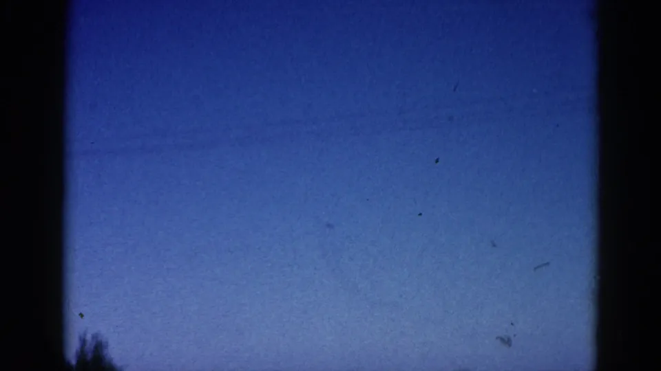 Clear blue sky occupies the frame as the 8mm clip ends, with dark vegetation barely entering at the lower left — consistent with a camera tilt upward at clip's end.