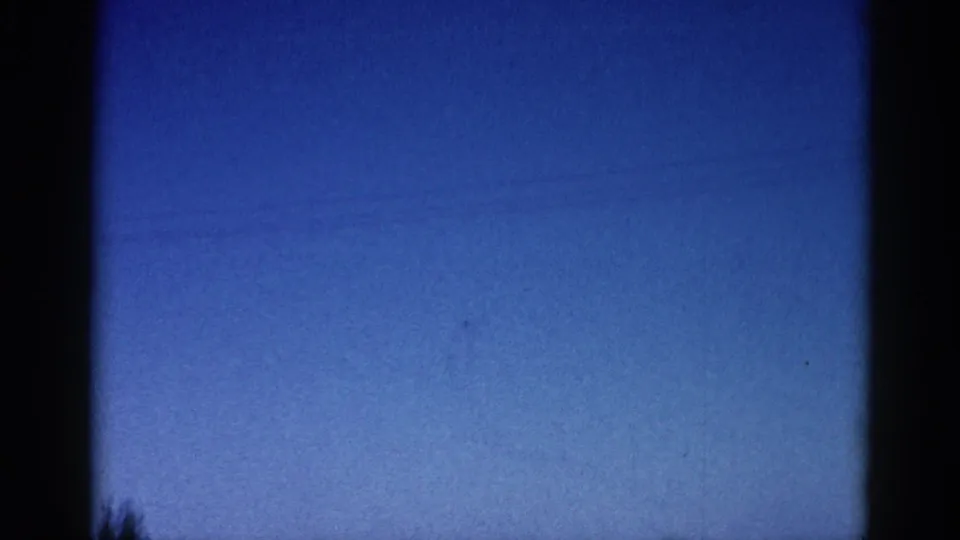 Trailing frame of an early 1960s 8mm home movie clip; blue sky dominates with possible treetops or power lines barely visible at the bottom edge.