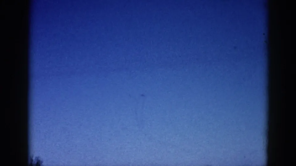 Final frame of an early 1960s 8mm home movie clip — blue sky with dark treetops at the lower edge, consistent with a camera tilt or end-of-roll exposure.