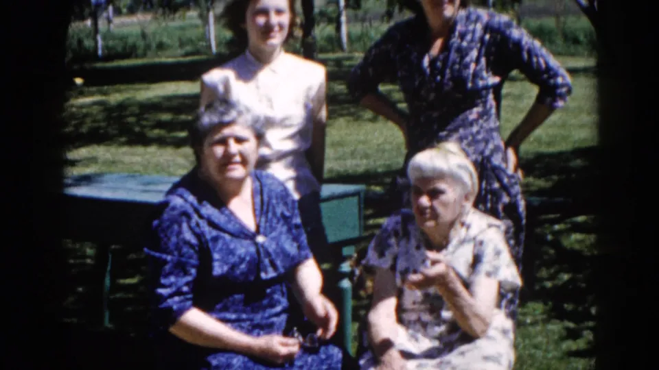 Closer view of three women from a multi-generational Illinois family group, c. 1962; elderly white-haired woman seated on a painted bench, flanked by two younger women.