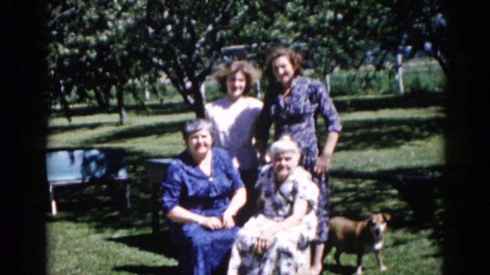 Multigenerational group of four women posing in a sunny Illinois backyard, 1962; a medium-sized brownish dog stands in the foreground grass.