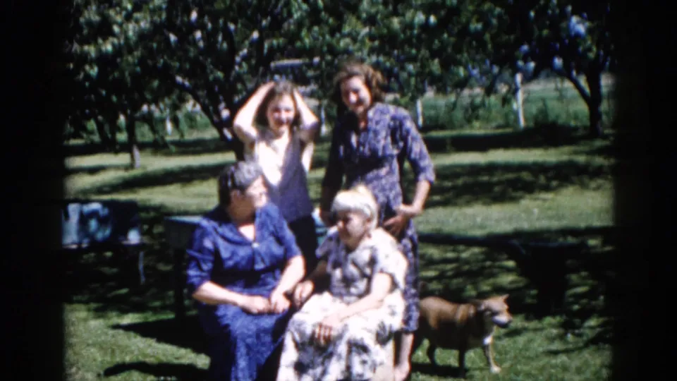 Multigenerational group of four women in an Illinois backyard, 1962; a medium dog at lower right and one woman with raised hand mark a candid moment.
