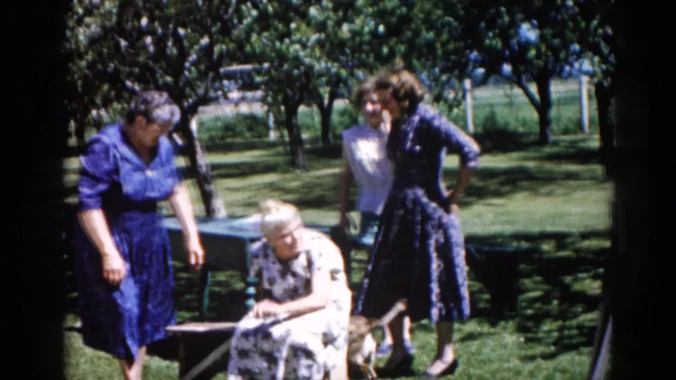 Four women gathered in a residential garden, likely Illinois circa 1962; one older woman seated at center with three others in period dresses standing nearby.