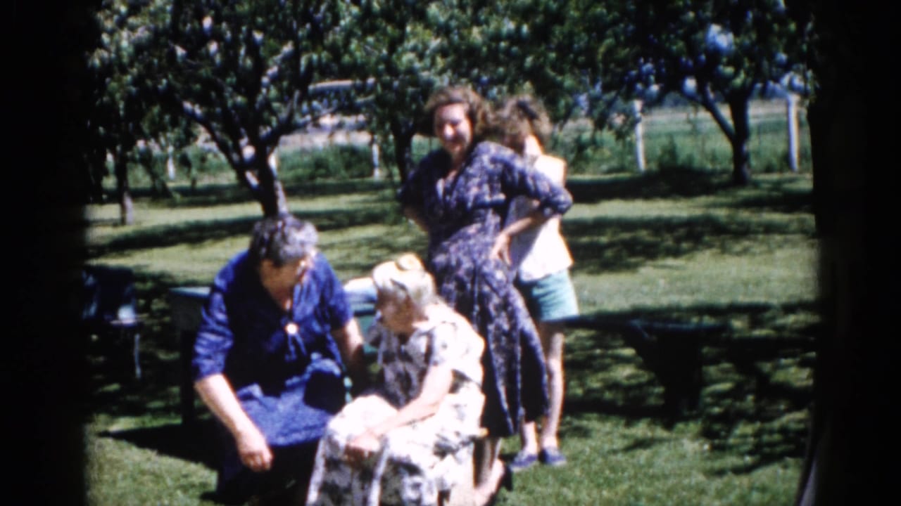 Women gathered in garden circa 1962; group composition shifts slightly; a smaller figure is visible at the right background edge, possibly a child.