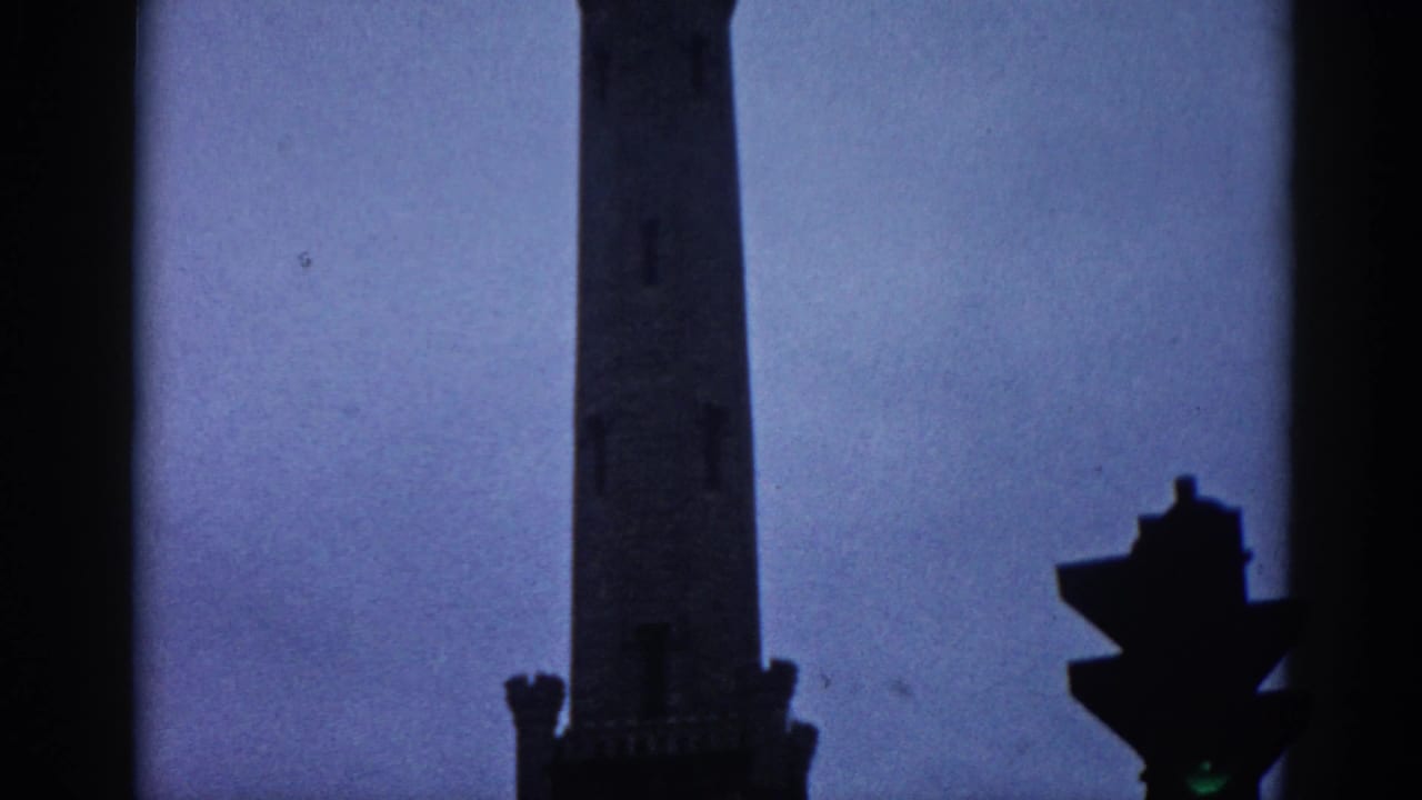 8mm home movie frame from 1962 Illinois showing a Gothic Revival building's upper tower rising against a dusky purple sky with a period traffic signal below.