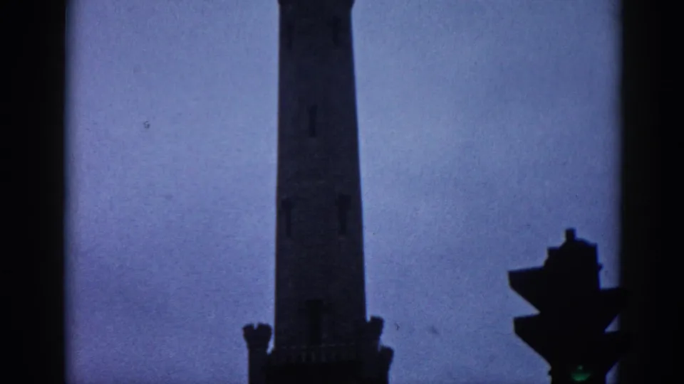 8mm home movie frame from 1962 Illinois showing a Gothic Revival building's upper tower rising against a dusky purple sky with a period traffic signal below.