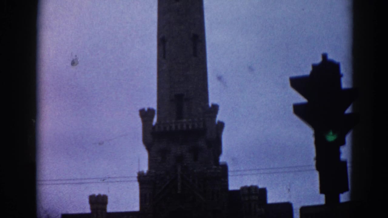 Gothic Revival building tower with crenellated battlements against a purple-grey sky; traffic light showing green at right edge; overhead utility lines visible.