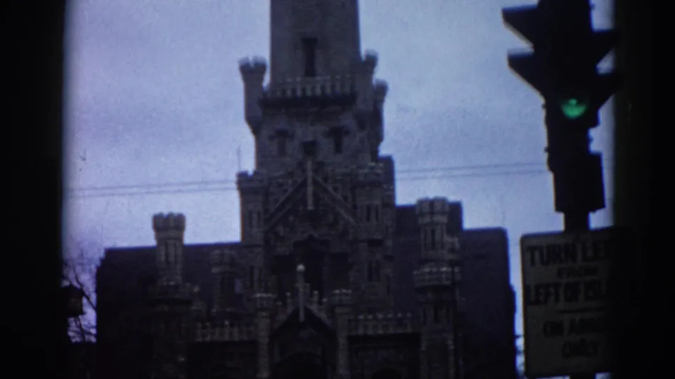 1962 Illinois 8mm footage showing a Gothic Revival building's facade with multiple towers, a period traffic signal, and a partially visible turn-restriction street sign.