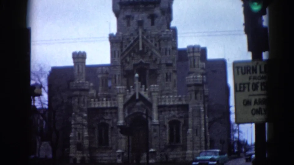 1962 Illinois 8mm home movie showing a full Gothic Revival building facade with central stone tower, period traffic signal, and turn-restriction sign reading 'TURN LEFT FROM LEFT OF ISLAND ON ARROW ONLY'.
