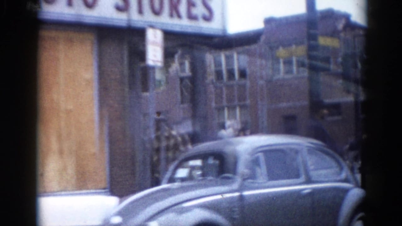 Volkswagen Beetle beside boarded-up brick storefronts, with a partial AUTO STORES sign visible above at street level.