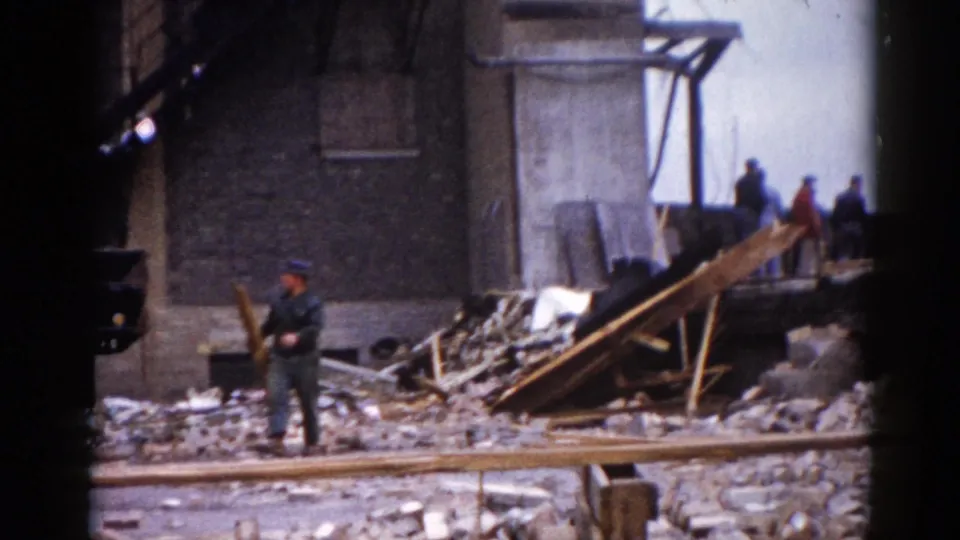 Demolition worker in mid-1960s period clothing amid brick and lumber rubble at the Illinois site circa 1962; additional crew members visible working in the background.