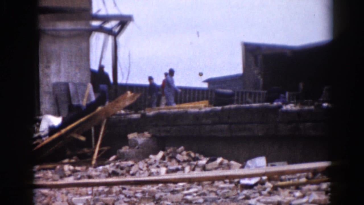Two or three workers navigate debris-strewn ground at what appears to be a 1962 Illinois demolition site, with broken bricks and angled lumber beams visible in the foreground.