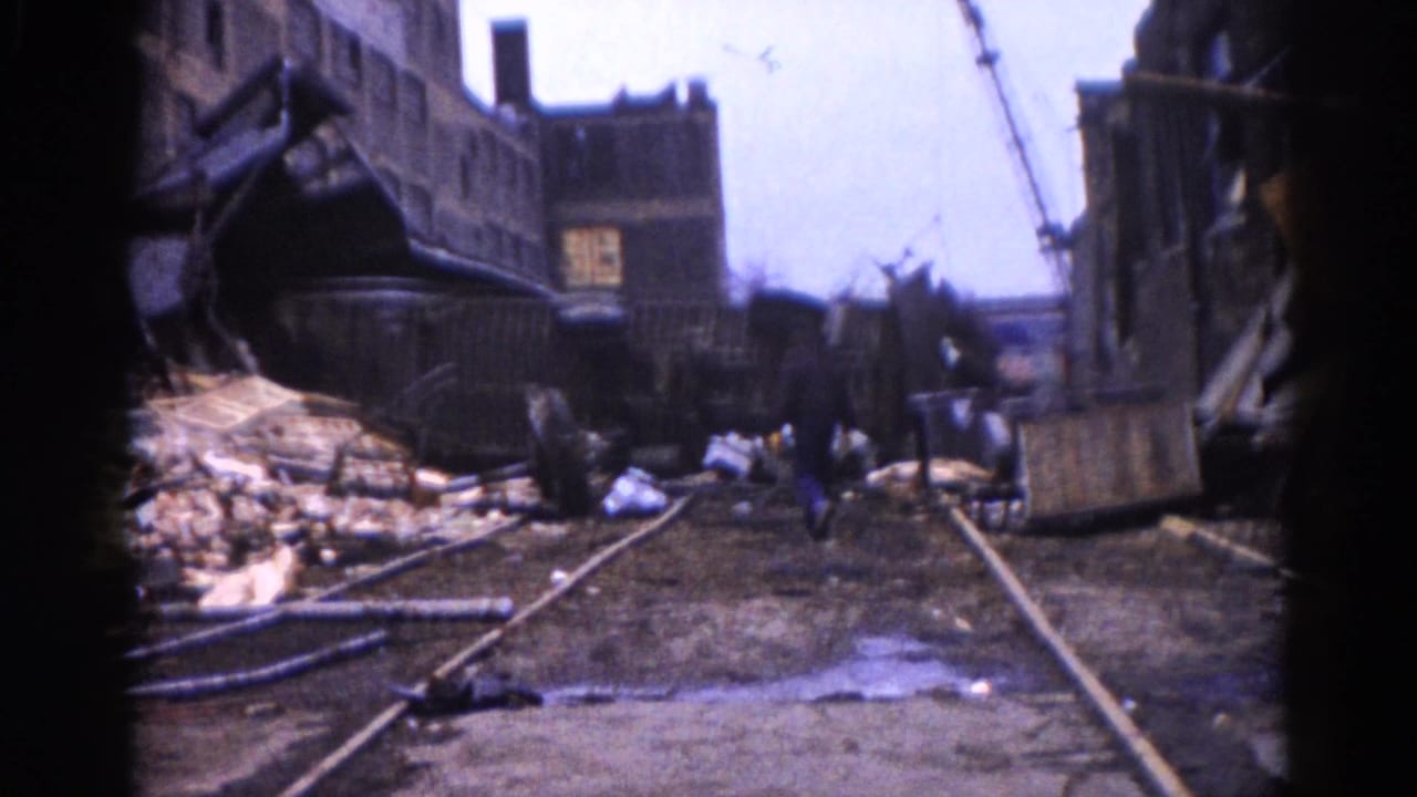 8mm color footage, c.1962 Illinois — railroad tracks cut through rubble toward damaged brick buildings and a crane under an overcast sky.