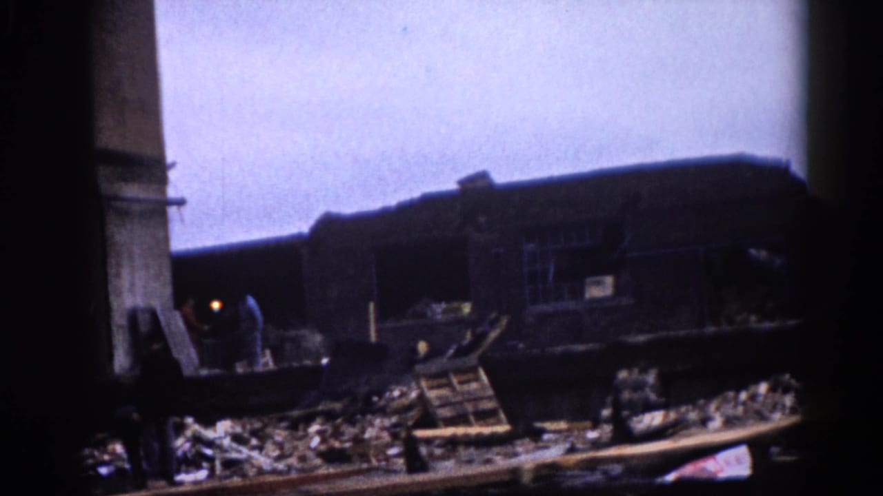 8mm color footage, c.1962: collapsed industrial building interior with timber and structural debris and a solitary figure visible amid the wreckage.