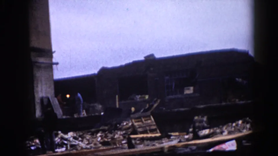8mm color footage, c.1962: collapsed industrial building interior with timber and structural debris and a solitary figure visible amid the wreckage.