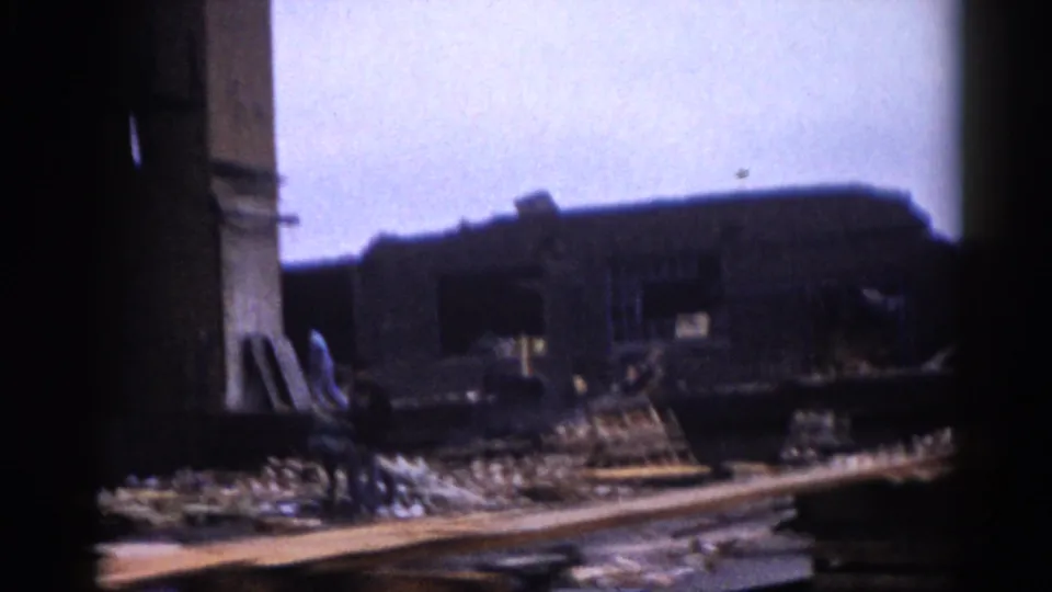 8mm color footage, c.1962, Illinois: wide ground-level view of industrial ruins with dark collapsed structures silhouetted against an overcast sky.