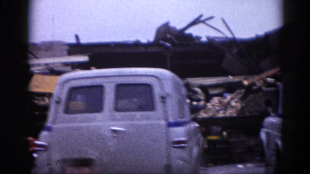 Rear view of a 1950s–1960s gray panel van beside collapsed building rubble in Illinois, circa 1962; 8mm color home movie.