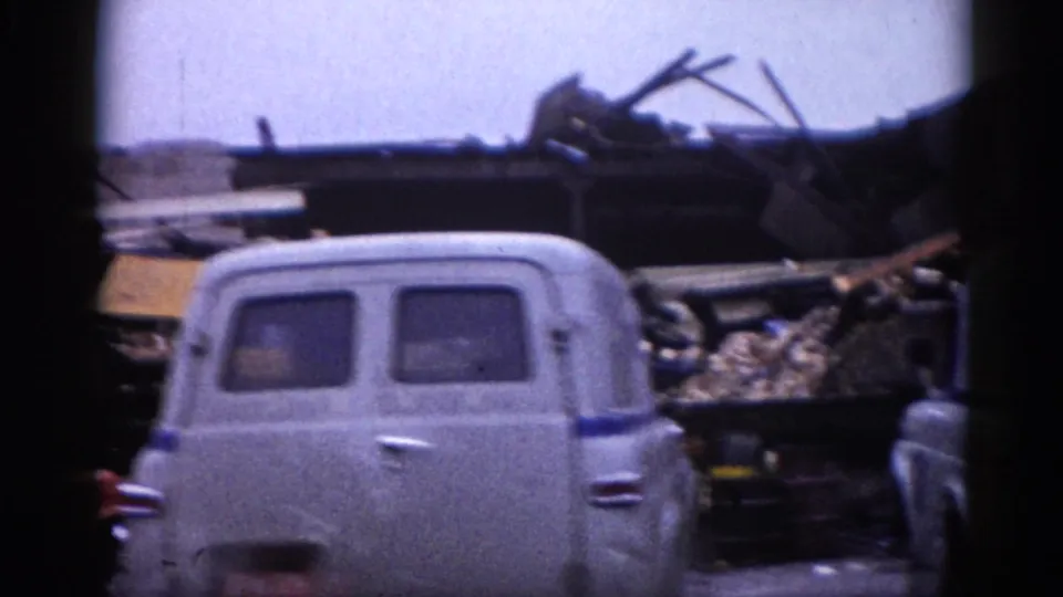 Rear view of a 1950s–1960s gray panel van beside collapsed building rubble in Illinois, circa 1962; 8mm color home movie.