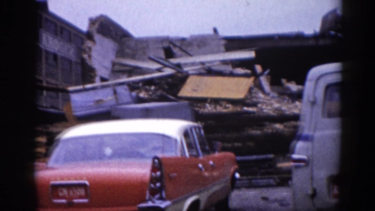 Rear view of a two-tone red-and-white American sedan with visible license plate parked near collapsed building debris, Illinois, circa 1962.
