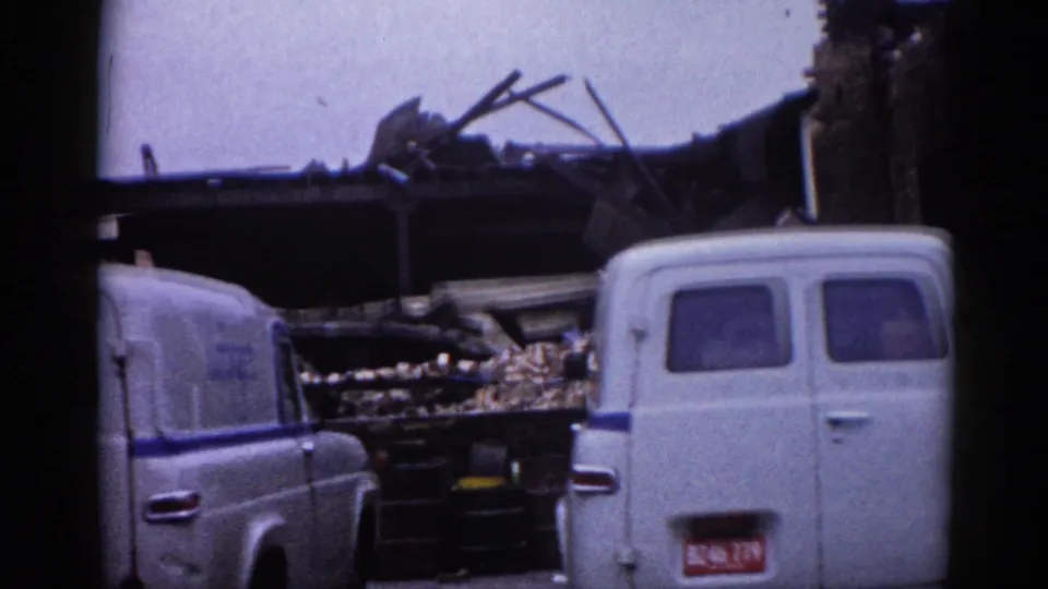 8mm home movie frame circa 1962 Illinois: white commercial work van beside collapsed building with timber debris and overcast sky; may document demolition or clearance activity.