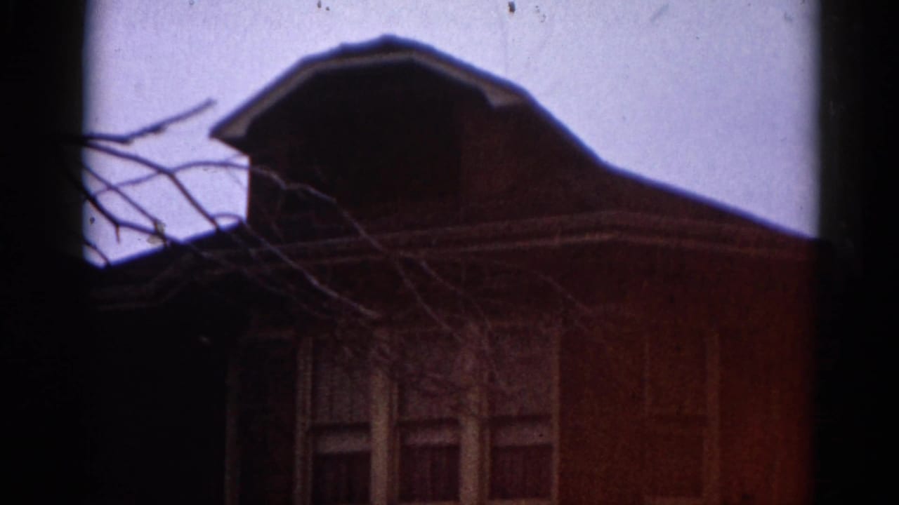 8mm film frame circa 1962 showing a brick residential house in Illinois; warm red cast and visible grain from aged emulsion.